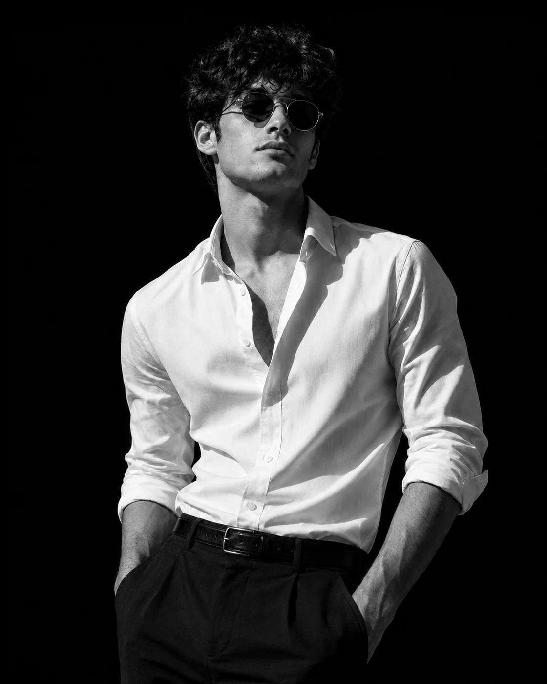 Monochrome Male Fashion Portrait AI Photo Editing Prompt. ChatGPT AI generated portrait of a stylish man wearing round sunglasses and an unbuttoned white shirt against a dark background.