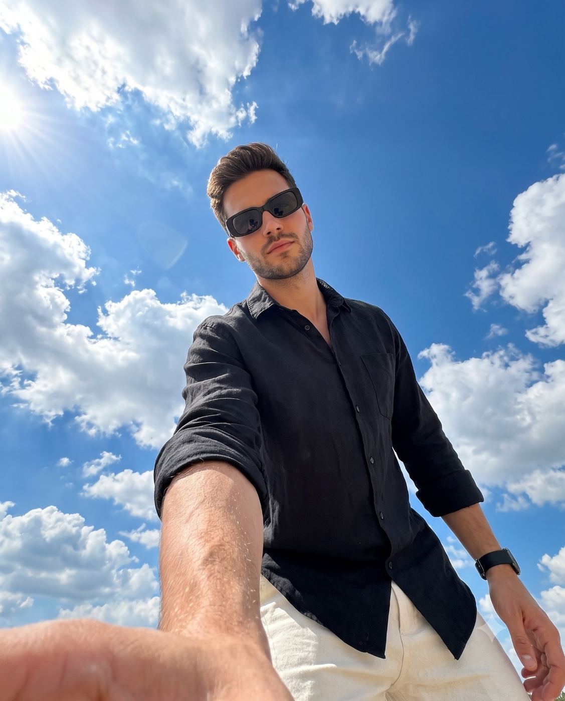 Low angle selfie portrait of man against blue sky AI Photo Editing Prompt. AI generated photorealistic portrait of a bearded man in sunglasses and a black shirt reaching toward the camera under a sunny sky.