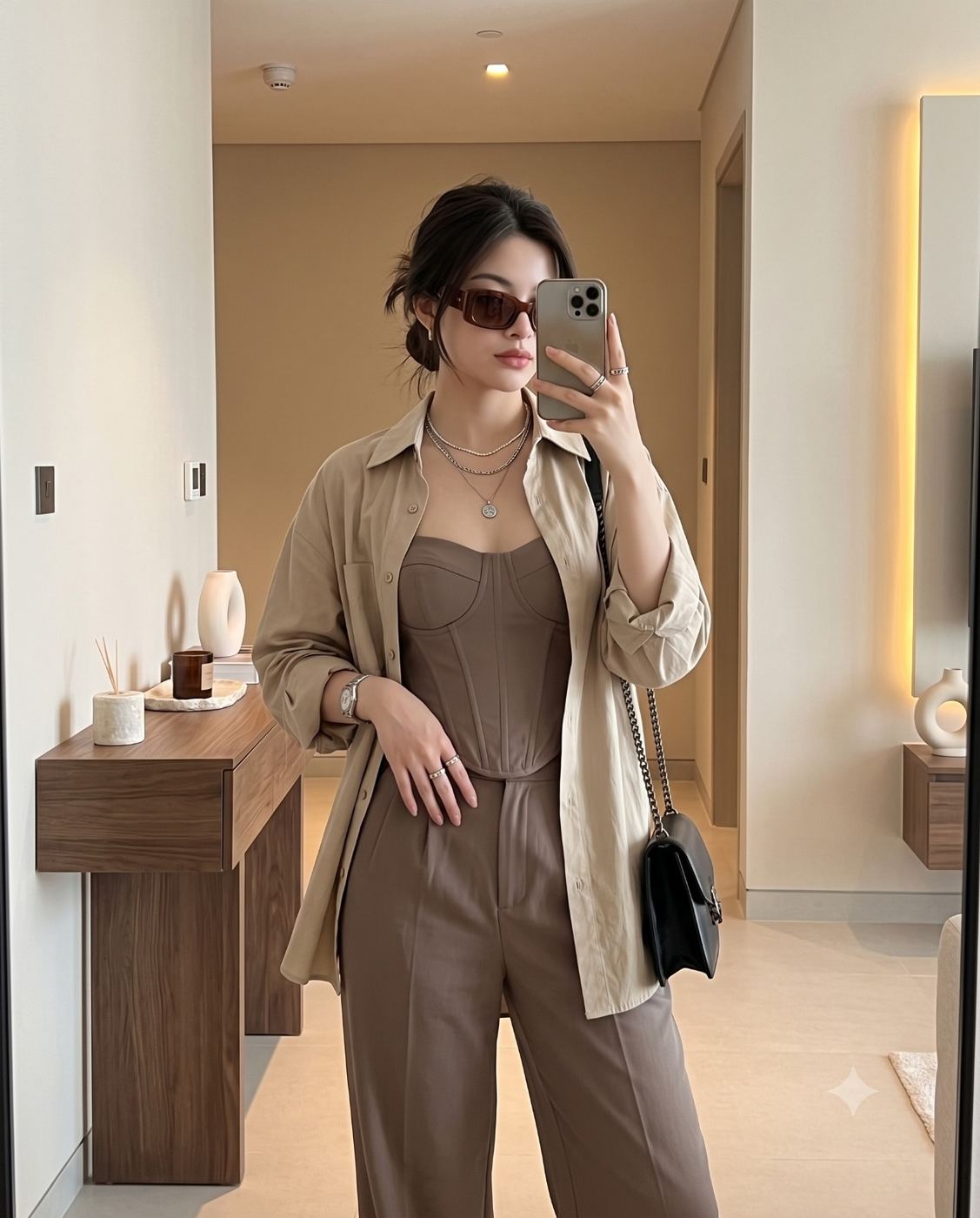 Chic neutral tone mirror selfie photography AI Photo Editing Prompt. AI generated lifestyle photograph of a stylish young woman wearing a brown corset top, beige shirt, and sunglasses taking a mirror selfie in a modern minimalist room.