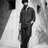 Gemini AI Photo Prompt: Ultra-detailed monochrome shot of a young man posing against a textured concrete corner illuminated by strong sunlight and tropical palm shadows.