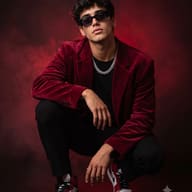 Dark Urban Style AI Photo Editing Prompt. AI generated studio portrait of a crouching young man in a red velvet blazer, sunglasses and chain against red fog.