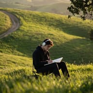 Gemini AI Photo Editing Prompt: Documentary style picture of a boy in a black hoodie writing in a notebook in a vast hillside meadow with blurred green grass.