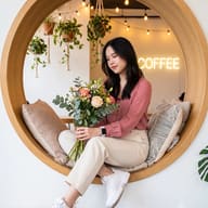 Cozy Cafe Portrait AI Photo Editing Prompt. AI generated lifestyle photo of a woman holding a floral bouquet in a circular wooden cafe window.