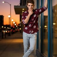 Urban Twilight Portrait of Boy AI Photo Editing Prompt. AI generated portrait of a stylish boy leaning against a glass window at dusk on a city sidewalk, wearing a maroon floral shirt and grey chinos.