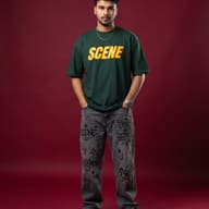 Young Indian Man in Green Graphic Tee and Graffiti Jeans Studio Portrait AI Photo Editing Prompt. AI generated studio portrait of a handsome bearded man wearing an oversized green t-shirt and printed grey jeans standing with hands in pockets against a solid maroon background.