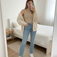 AI generated realistic portrait of a young woman taking a mirror selfie in a bright, modern bedroom, wearing a beige tank top, cream hoodie, and light-washed blue jeans.