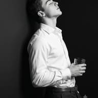 Man Black and White Portrait AI Prompt. AI generated studio portrait of a young man with closed eyes, wearing a white shirt and holding a glass against a black wall.
