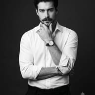AI generated studio portrait of a man in crisp white shirt with rolled-up sleeves in a thoughtful pose, touching his chin with arms crossed and wearing a watch, against a dark background.