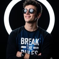 Smiling young man in round Ray-Ban style mirrored sunglasses and a "Break The Rules" sweatshirt, arms crossed, standing before a glowing white neon ring light on a black background — AI generated portrait photo editing prompt by Promptplum.