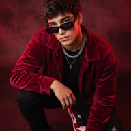 AI generated studio portrait of a young man crouching in a red velvet jacket and sunglasses against a smoky red background.