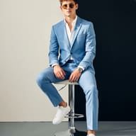 Gemini AI Generated Premium photoshoot picture of a young man with curly hair and sunglasses dressed in a tailored blue suit and white shirt.