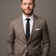 AI Photo Prompt: Premium corporate headshot of a smiling man with a short beard wearing a taupe suit and black tie against a gray studio background