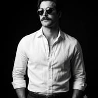 Monochrome Male Fashion Portrait AI Photo Editing Prompt. Gemini AI generated portrait of a stylish man wearing round sunglasses and an unbuttoned white shirt against a dark background.