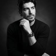 Gemini AI generated Cinematic monochrome studio shot of a bearded man with a steel wristwatch posing thoughtfully.