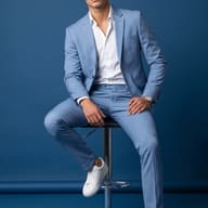 Gemini AI Prompt: Editorial fashion picture of a stylish man in a powder blue suit and white sneakers sitting on a chrome stool in a blue studio.