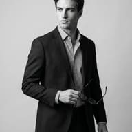 Man Fashion Editorial Prompt. AI-generated black and white studio portrait of a handsome man in a dark suit and striped shirt, looking away while holding eyeglasses.