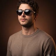 Brown Studio Photo AI Prompt. AI generated portrait of a curly-haired man in round sunglasses and a beige sweater against a warm brown backdrop."