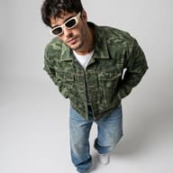 Streetwear Male Portrait AI Photo Editing Prompt. AI generated studio portrait of a trendy bearded man wearing a camouflage denim jacket, retro white sunglasses, and baggy jeans captured from a high-angle perspective.
