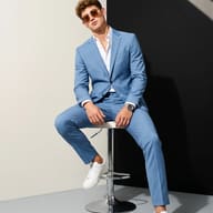 AI Photoshoot Prompt: Stylish menswear campaign picture of a guy in a light blue suit and shades resting on a chrome bar stool.