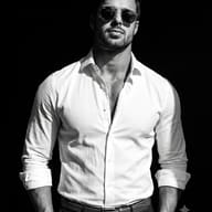 Monochrome Fashion Portrait AI Prompt. AI generated studio portrait of a bearded man wearing round sunglasses and a white shirt against a black background.