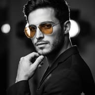 AI Image Prompt: Black and white studio picture of a man with a beard wearing amber aviator sunglasses and a dark jacket.