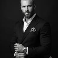 Black and White Portrait of Man in Suit AI Photo  Prompt. AI generated studio portrait of a well-groomed man wearing a dark double-breasted suit, paisley pocket square, and adjusting his wristwatch.