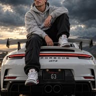 ChatGPT Image Prompt: Cinematic Moody automotive lifestyle portrait of a stylish man sitting on the back of a white Porsche 911 GT3 with a dark stormy sky in the background.