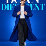 ChatGPT AI Generated Stylish fashion photography of a young male model holding his coat lapels while walking against a saturated blue backdrop featuring bold text.