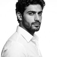 AI generated black and white portrait of a handsome bearded man in a white collared shirt, viewed in profile, with a direct and intense gaze against a white background.