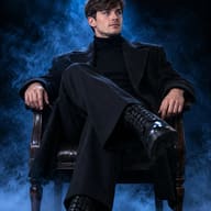 ChatGPT AI Generated High-contrast fashion portrait of a serious young man in a dark wool coat and leather boots sitting under a cool blue spotlight.