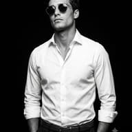 AI generated studio portrait of a stylish man wearing round sunglasses, a crisp white shirt, and dark trousers against a black background.