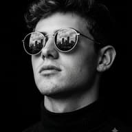 AI Image Prompt: Moody monochrome fine-art close-up of a young man wearing round sunglasses with sharp reflections of skyscrapers and clouds against a pure black background.