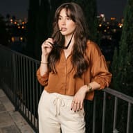 Aesthetic Rooftop Portrait AI Photo Editing Prompt. AI generated fashion portrait of a woman in a brown satin blouse holding sunglasses against city lights.