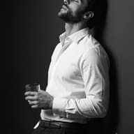 Fine Art Portrait AI Photo Editing Prompt. AI generated black & white image of a man leaning on a wall holding a glass.