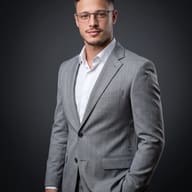 AI Photo Prompt: Three-quarter business portrait of a handsome man wearing rectangular glasses and a light gray check suit in a professional photography studio.