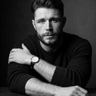 Classic Black and White Man Portrait AI Photo Editing Prompt. AI generated portrait of a rugged bearded man in a black knit sweater, arms crossed on a table, wearing a wristwatch in dramatic monochrome studio lighting.