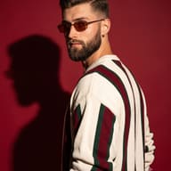Editorial Portrait of Bearded Man in Striped Knit and Sunglasses AI Photo Editing Prompt. AI generated studio portrait of a man with sunglasses over his shoulder in a cream, red, and green striped knit sweater on a deep red background with a dramatic shadow.