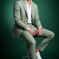AI Image Prompt: Young man wearing a light green suit posing on a stool in a green studio setup.