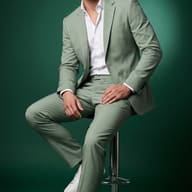 Gemini AI Photo Prompt: Handsome man in a green menswear suit and white sneakers seated on a bar stool.