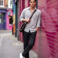 Urban Street Style Photography AI Prompt. AI generated portrait of a stylish man in a grey shirt and black trousers leaning against a pink brick wall.