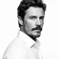 High-Contrast Monochrome Portrait AI Photo Editing Prompt. AI generated studio portrait of a man with textured dark hair, mustache, and a short beard, wearing a white collared dress shirt against a white background