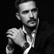 Man in Suit AI Photo Editing Prompt. AI generated B&W studio portrait of a man with a prominent mustache and luxury watch, featuring dramatic lighting and a sharp suit.