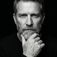 Thoughtful Mature Man AI Photo Editing Prompt. AI generated black and white studio portrait of a pensive bearded man resting his hand on his chin against a dark background.
