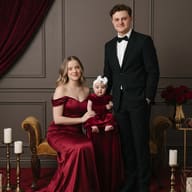 Elegant Formal Studio Family Portrait AI Photo Editing Prompt. AI generated studio portrait of a woman in a red satin gown, a man in a tuxedo, and a baby in a velvet dress on a gold lounge with candles and roses.