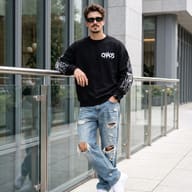 Urban Streetwear Fashion Portrait AI Photo Editing Prompt. AI generated outdoor portrait of a stylish young man wearing a black "CHAOS" sweatshirt, ripped jeans, and sunglasses leaning against a glass railing in a modern city setting.