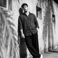 Gemini Generated Cinematic black and white portrait of a man in a linen shirt leaning against a concrete wall with sharp palm tree shadows.