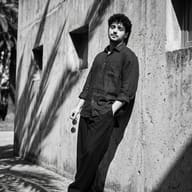 AI Prompt: Black and white summer editorial shot of a young man with a casual outfit leaning relaxed against a concrete building facade.