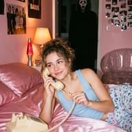 Gemini AI Photo Prompt: Nostalgic Y2K bedroom scene showing a smiling girl in a blue top on a pink bed with a corded phone, while Ghostface stands in the dark background.