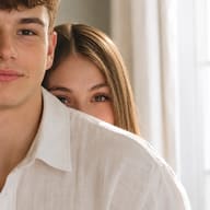 Candid couple photography AI photo editing prompt. AI generated portrait of a boyfriend in a white shirt with his girlfriend playfully peeking behind his collar.