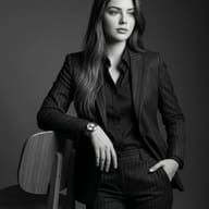 AI generated monochrome studio portrait of a businesswoman in a dark pinstripe suit leaning on a wooden chair.